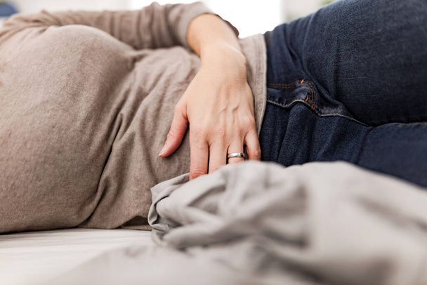 Unavená vyčerpaná žena s žaludečními potížemi doma na gauči, nemocná, těhotná. - Fotografie, Obrázek