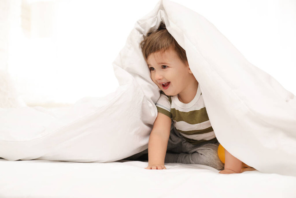 Cute little child playing under blanket in bed - Valokuva, kuva
