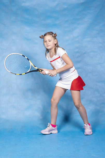 青い背景で試合前にウォーミングアップする若いテニス選手。テニス、レセプション、子供スポーツ. - 写真・画像