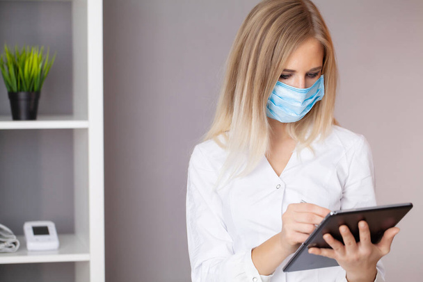 Vrouwelijke arts met beschermend masker aan het werk op tablet op kantoor - Foto, afbeelding