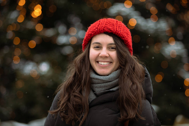 Portret pięknej uśmiechniętej kobiety w czerwonym kapeluszu choinki na tle. strój zimowy - Zdjęcie, obraz