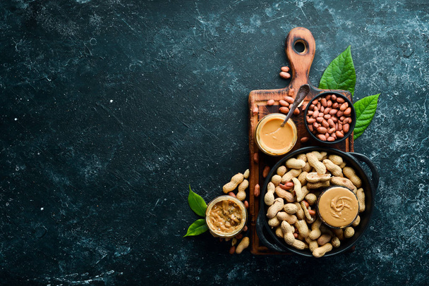 Peanut butter and nuts on a black stone background. Healthy food. Top view. - 写真・画像