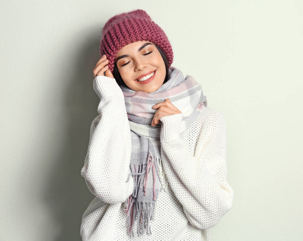 Young woman wearing warm sweater, scarf and hat on light background. Winter season - Zdjęcie, obraz