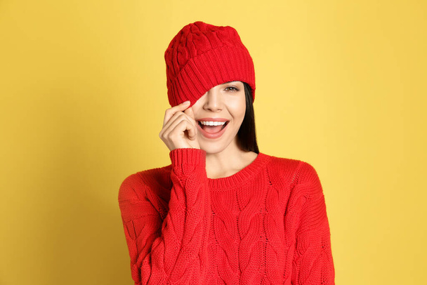 Young woman wearing warm sweater and hat on yellow background. Winter season - Foto, Imagen