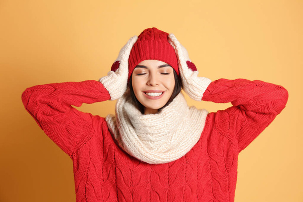 Young woman wearing warm sweater, scarf, mittens and hat on yellow background. Winter season - Foto, immagini