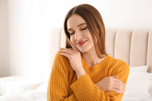 Young woman wearing warm sweater on bed at home. Winter season - Фото, зображення