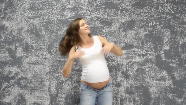 Kaunis nuori raskaana oleva tyttö tanssii taustalla harmaa seinä kotona
 - Materiaali, video