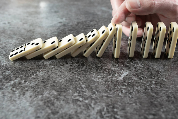 close-up van mannelijke hand voorkomen dat lijn van domino tegels omvallen en omvallen - Foto, afbeelding