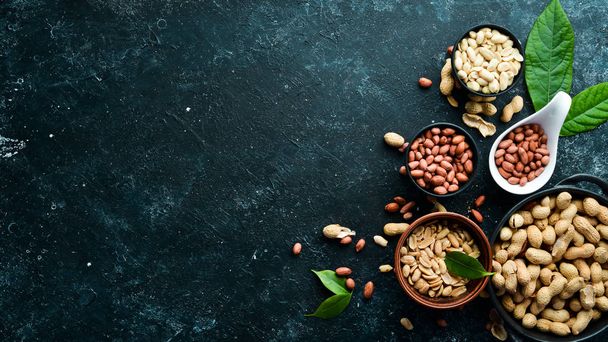 Set of peanuts in bowls on a black stone background. Nut background. Top view. - 写真・画像