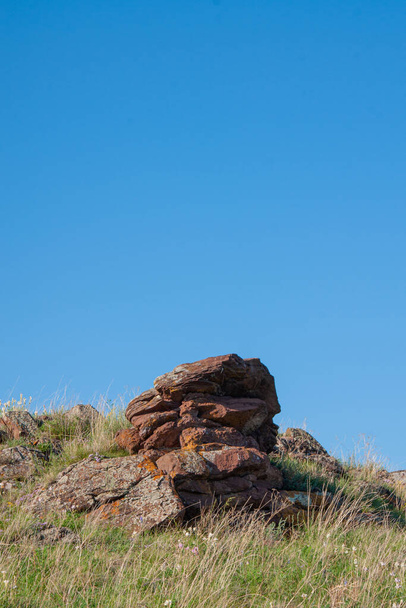 Μέρος ενός λόφου με ένα βράχο που προεξέχει από αυτό σε ένα μπλε ουρανό. Κοντινό πλάνο σε μια ηλιόλουστη καλοκαιρινή μέρα. - Φωτογραφία, εικόνα