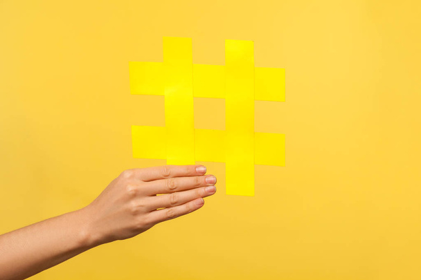 Closeup of female hand holding big large yellow hashtag symbol of internet trends, hash sign, blogging and popularity in social media network. isolated on yellow background, isolated studio shot - Foto, afbeelding
