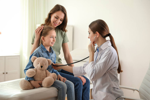 Mother and daughter visiting pediatrician. Doctor examining little patient with stethoscope in hospital - 写真・画像