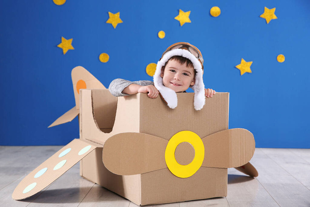 Cute little child playing with cardboard airplane near blue wall - Foto, Imagen