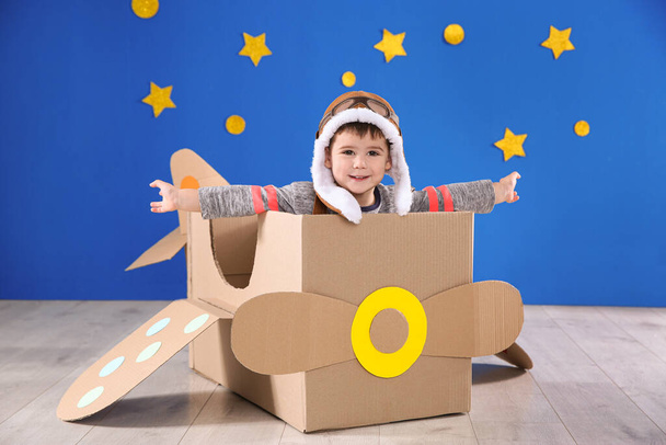 Cute little child playing with cardboard airplane near blue wall - Foto, Imagem