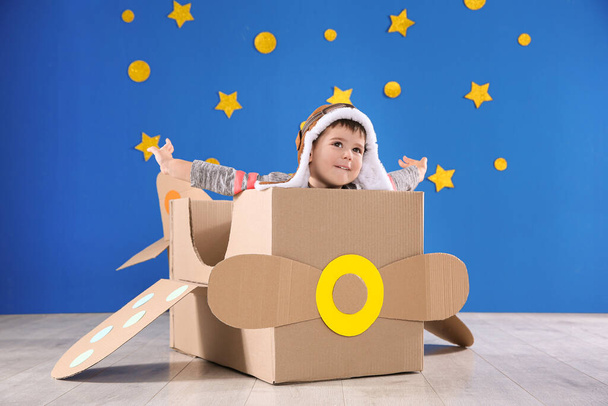 Cute little child playing with cardboard airplane near blue wall - Zdjęcie, obraz
