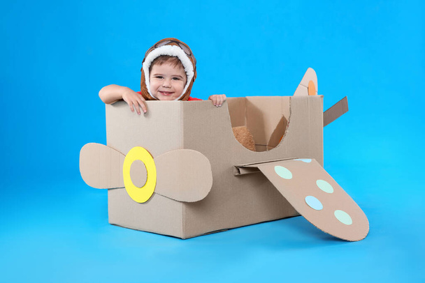 Cute little child playing with cardboard airplane on light blue background - Valokuva, kuva