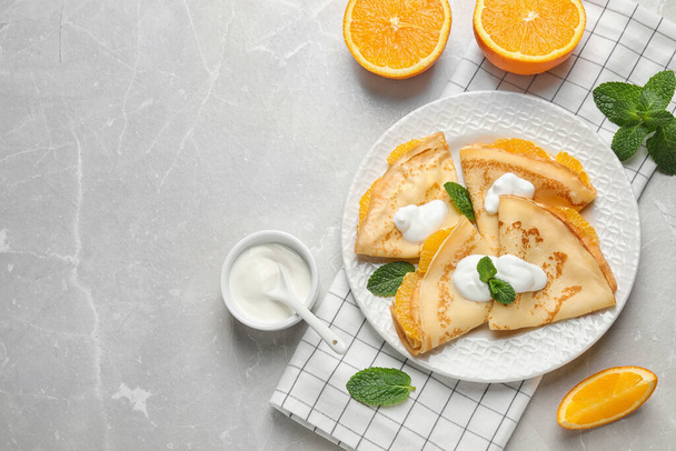 Delicious thin pancakes with oranges and cream on marble table, flat lay. Space for text - Foto, Imagen