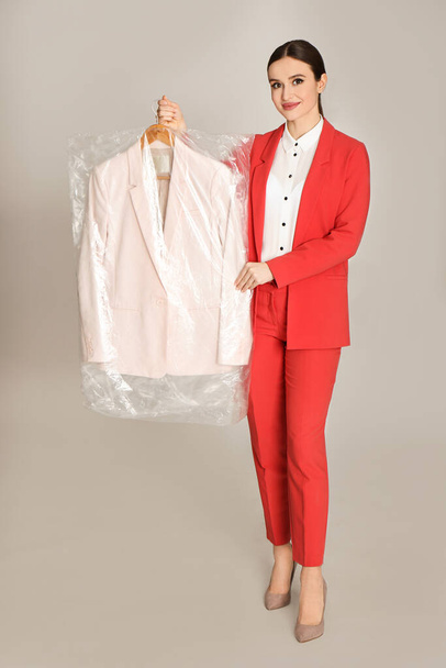 Young woman holding hanger with jacket on light grey background. Dry-cleaning service - Photo, Image