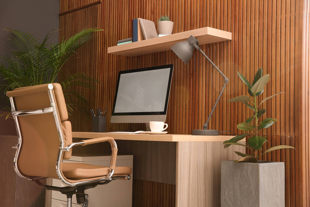 Comfortable workplace with computer near wooden wall in stylish room interior. Home office design - Photo, Image