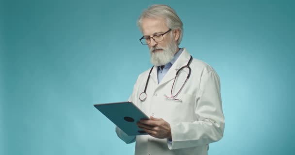 Elektronik tabletini kullanırken kameraya bakan dost canlısı bir doktorun portresi. - Video, Çekim
