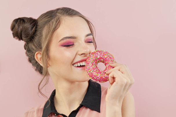 Šťastná hezká dívka drží koblihu na růžovém pozadí, módní portrét - Fotografie, Obrázek