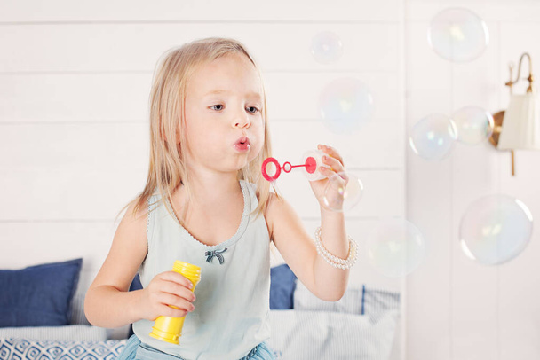 Portrait of funny little girl blowing bubbles at home - Фото, изображение
