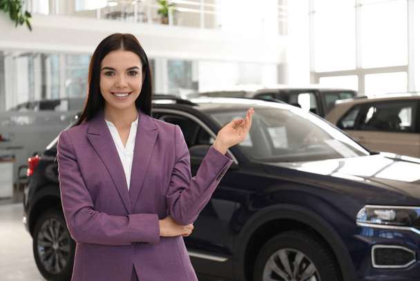 Happy young saleswoman in modern car salon - Фото, изображение