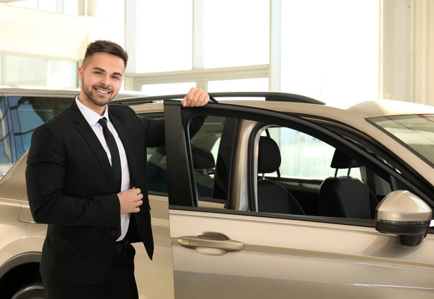 Young salesman near new car in dealership - Foto, afbeelding