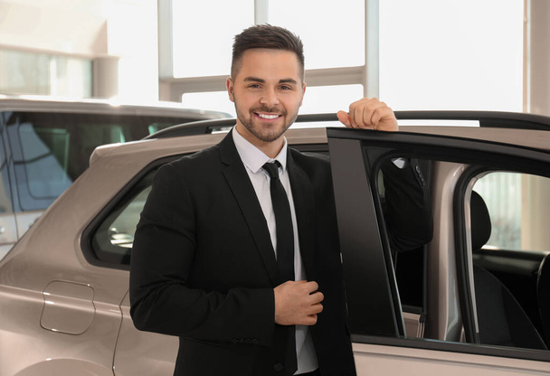 Young salesman near new car in dealership - Fotografie, Obrázek
