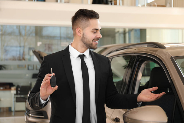 Young salesman with key near car in dealership - 写真・画像