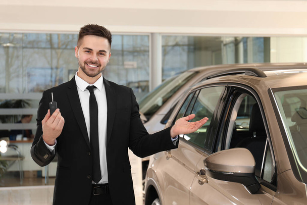 Young salesman with key near car in dealership - 写真・画像