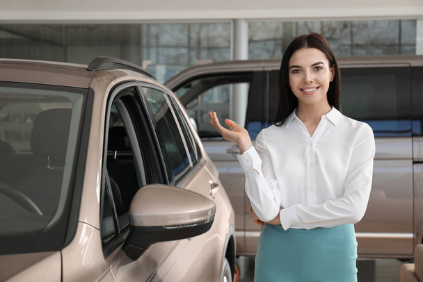 Young saleswoman near new car in dealership - Foto, afbeelding