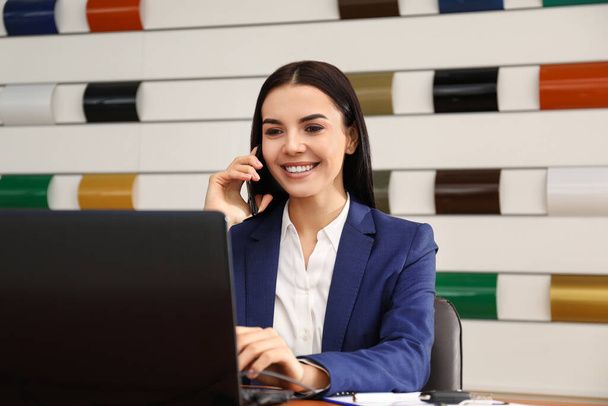Saleswoman talking on phone at desk in car dealership - Zdjęcie, obraz
