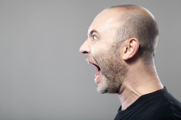 Портрет разъяренного мужчины, кричащего на сером фоне
 - Фото, изображение