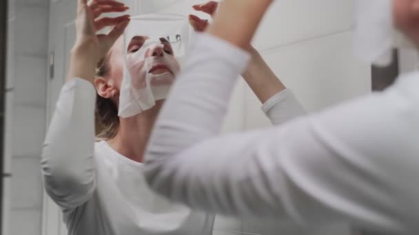 Woman removes mask on her face looking in mirror - Footage, Video