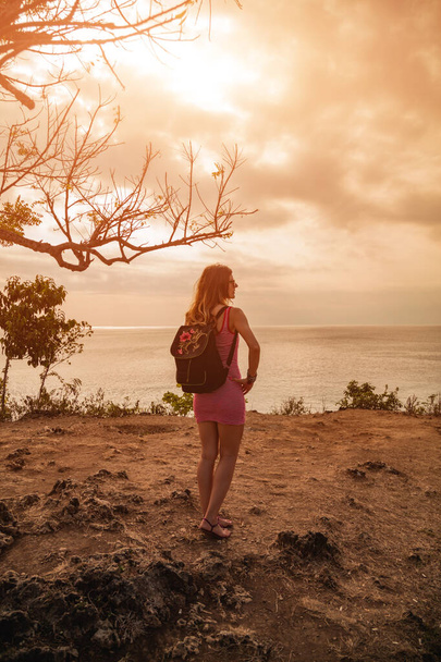 Женщина смотрит на далёкий морской пейзаж с высокой скалы океана
. - Фото, изображение