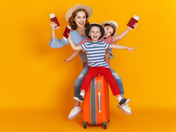 ¡Feliz viaje! familia de viajeros madre e hijos con entradas maletas y pasaportes en el fondo amarillo de color
 - Foto, Imagen