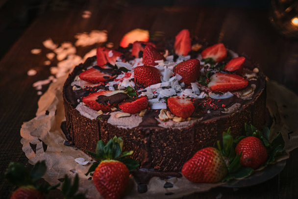 Vegan and delicious chocolate cake with strawberries, cocnut shovel and raspberry seeds, served on a paper serviette - Foto, immagini