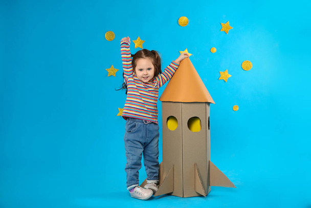 Little child playing with rocket made of cardboard box near stars on blue background - Fotoğraf, Görsel
