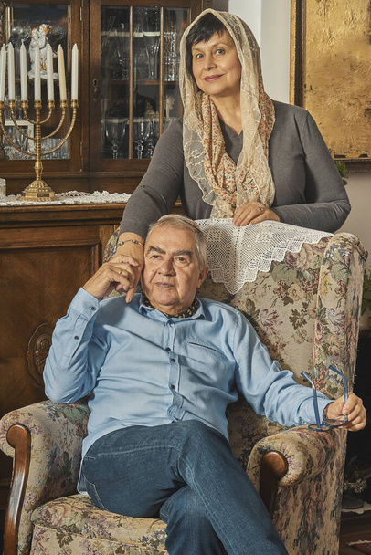 Εβραϊκό ηλικιωμένο ζευγάρι ποζάρει στην πολυθρόνα στο παραδοσιακό σπίτι  - Φωτογραφία, εικόνα