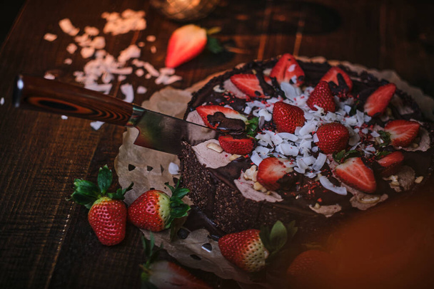 Vegan chocolate cake with strawberries, cocnut shovel and raspberry seeds, served on a paper serviette - Zdjęcie, obraz