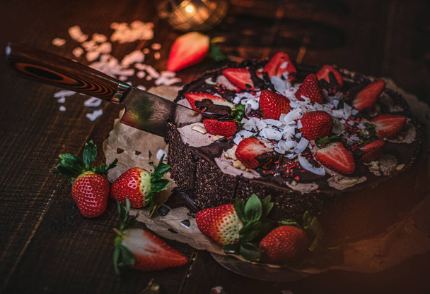 Vegan chocolate cake with strawberries, cocnut shovel and raspberry seeds, served on a paper serviette - Foto, Bild
