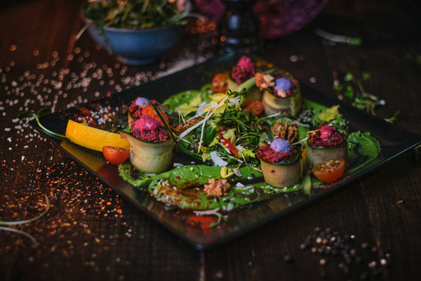 Cozinha alta prato vegetariano de rolos de aperitivo e uma tigela de ervas servidas em uma mesa de madeira ao lado de moedor de sal em um restaurante
 - Foto, Imagem
