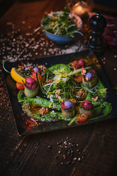 Placa vegetariana crua de rolos de aperitivo e uma tigela de ervas servidas em uma mesa de madeira ao lado de moedor de sal em um restaurante
 - Foto, Imagem
