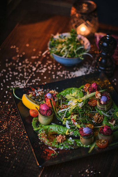 Platillo vegetariano de alta cocina con rollos de aperitivo y un tazón de hierbas servido en una mesa de madera junto a la picadora de sal en un restaurante
 - Foto, imagen