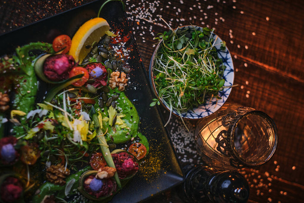 Piatto vegetariano crudo di involtini di antipasto e una ciotola di erbe servite su un tavolo di legno accanto al macinino di sale in un ristorante
 - Foto, immagini