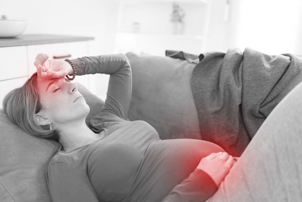 Schwangere müde erschöpfte Frau mit Magen- und Kopfproblemen zu Hause auf der Couch, krank. - Foto, Bild