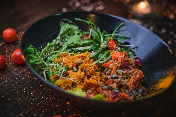 Tasty vegetarian bowl of plov served on a wooden table decorated with spices in a dark soft light of a restaurant - 写真・画像