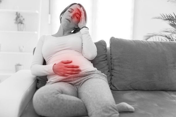 Ciężarne zmęczona kobieta z problemami żołądka i głowy w domu na kanapie, jest chory. - Zdjęcie, obraz