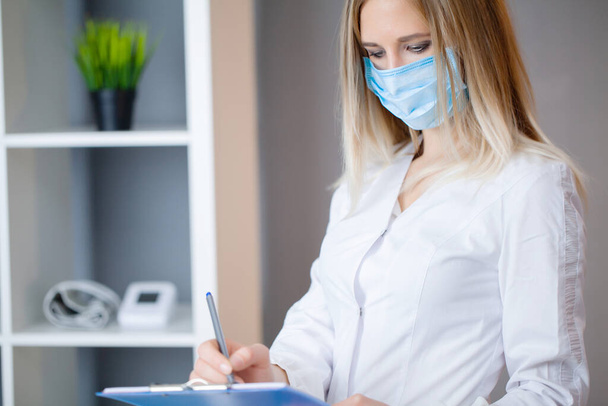 Ärztin mit Schutzmaske arbeitet im Büro an Tablet - Foto, Bild